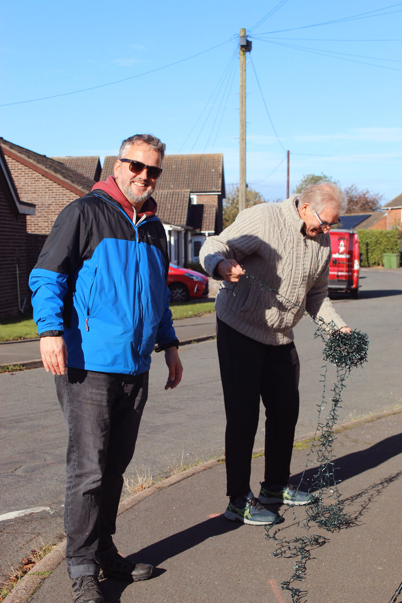 Two people untangling Christmas lights on a residential street
