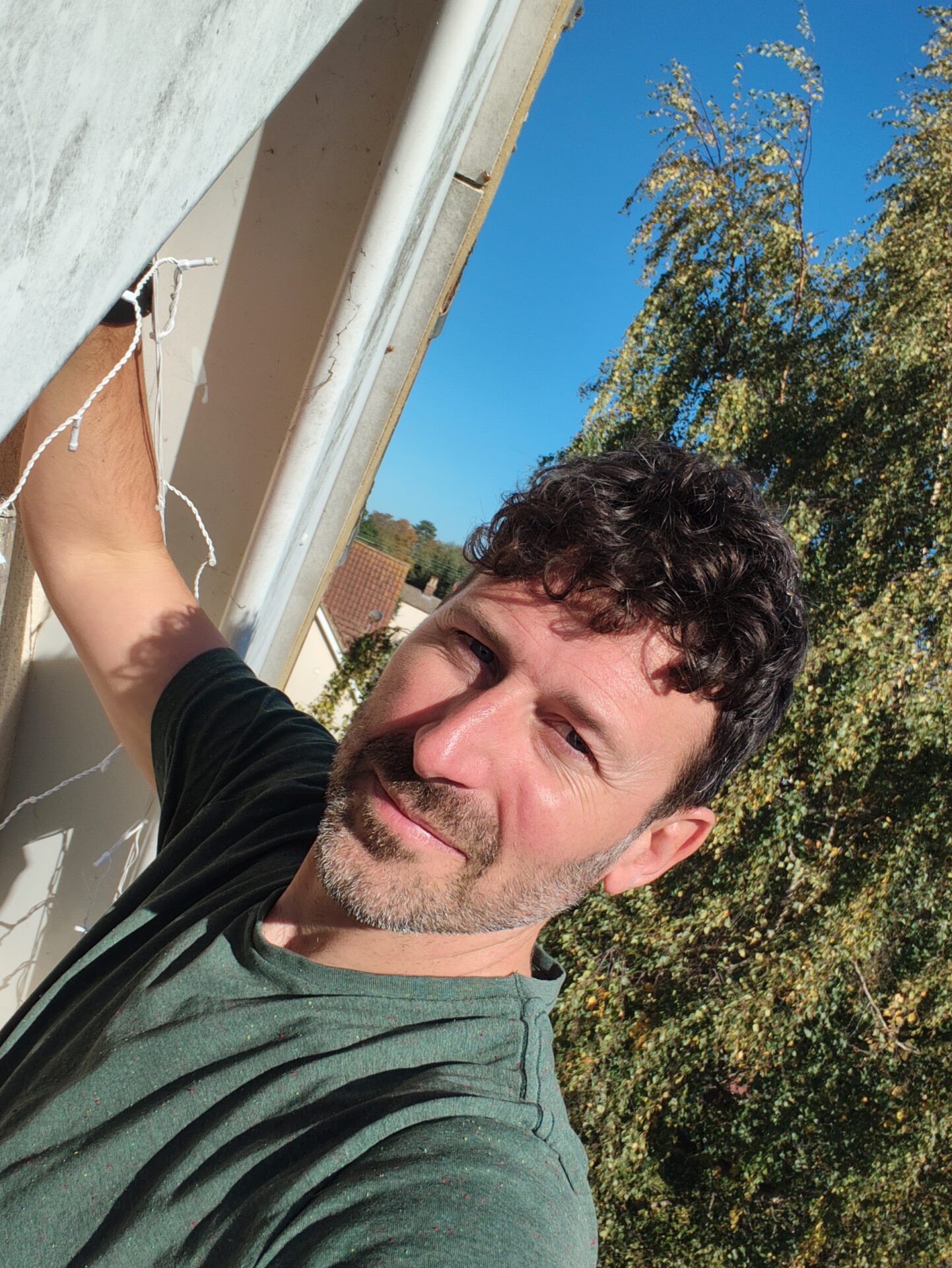 Man smiling whilst installing fairy lights on house exterior